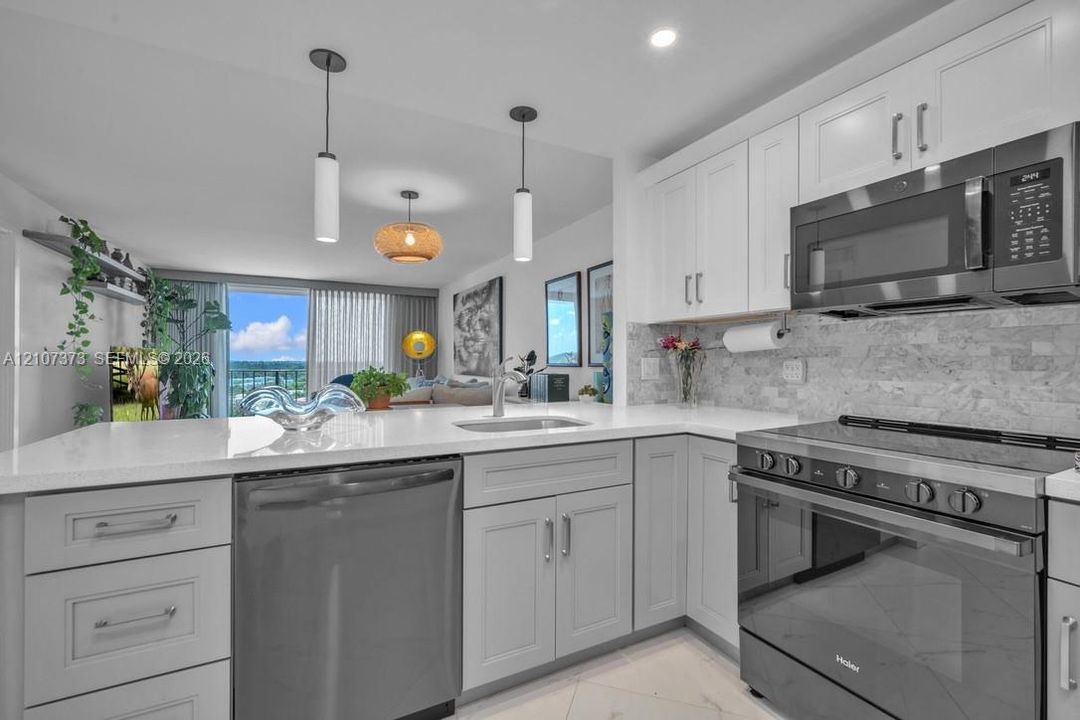 Kitchen featuring white shaker-style cabinetry, quartz countertops, stone tile backsplash, stainless steel appliances, and dual pendant lighting