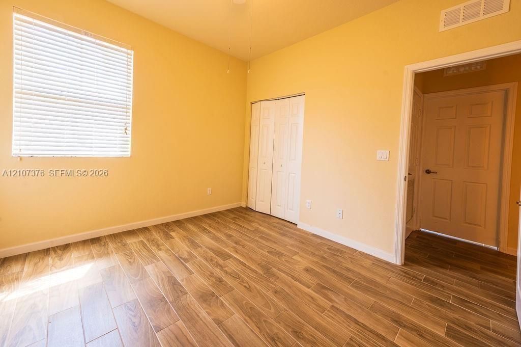 Room featuring wood-finish tile flooring, a window with installed horizontal blinds, and a built-in closet with bi-fold doors