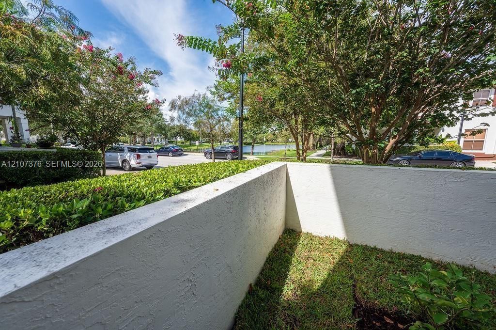 Private outdoor space featuring a textured stucco privacy wall, manicured perimeter shrubbery, and a small grass lawn