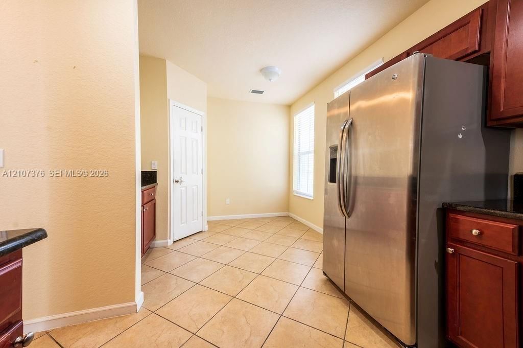 Kitchen area featuring ceramic tile flooring, stainless steel side-by-side refrigerator, cherry-finish cabinetry, and stone-finish countertops