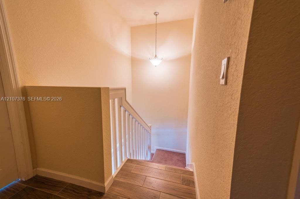 Staircase featuring wood-finish flooring, white painted railing, and a pendant light fixture