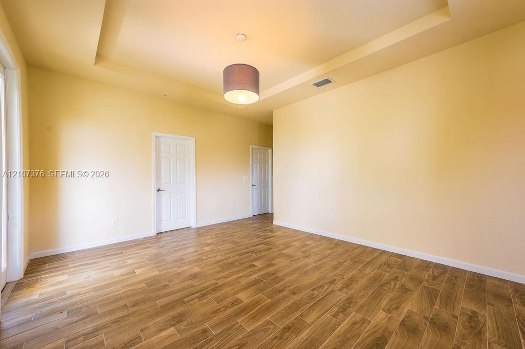 Tray ceiling featuring a central drum pendant light fixture, paired with wood-finish flooring and solid-core six-panel interior doors