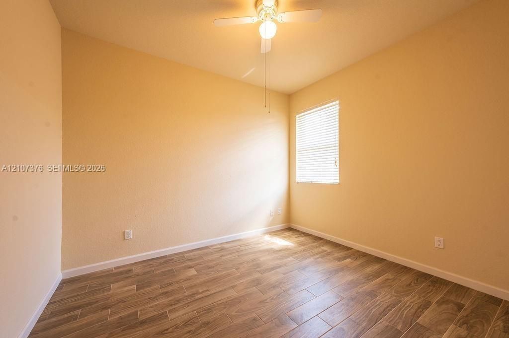Room featuring wood-finish tile flooring, textured wall finishes, and a central ceiling fan with integrated lighting