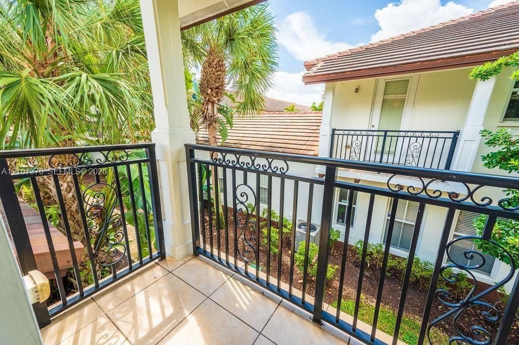 Private balcony featuring decorative wrought-iron railings, tiled flooring, and mature tropical landscaping