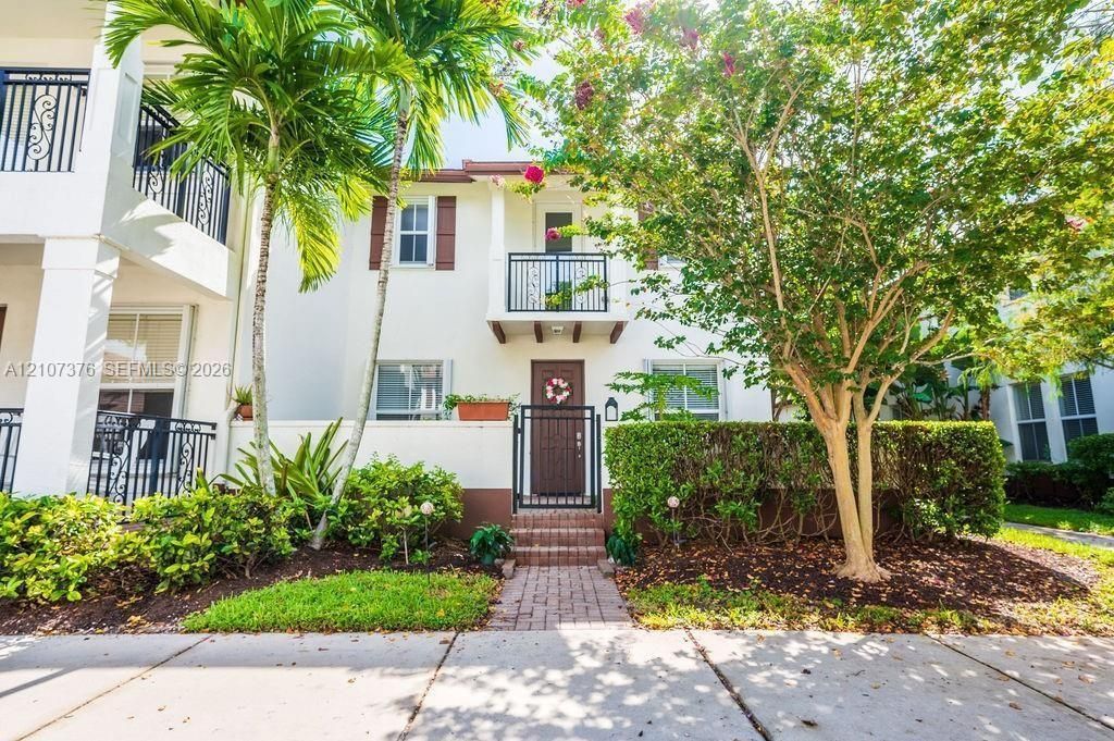 Multi-story exterior featuring a light-toned stucco façade, decorative metal balcony railings, a private gated courtyard entry, and a paver walkway