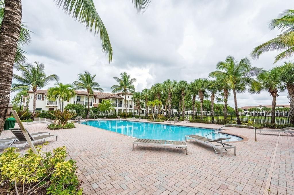 Community swimming pool featuring a rectangular basin with metal handrails, surrounding herringbone-patterned paver decking, and mature palm tree landscaping