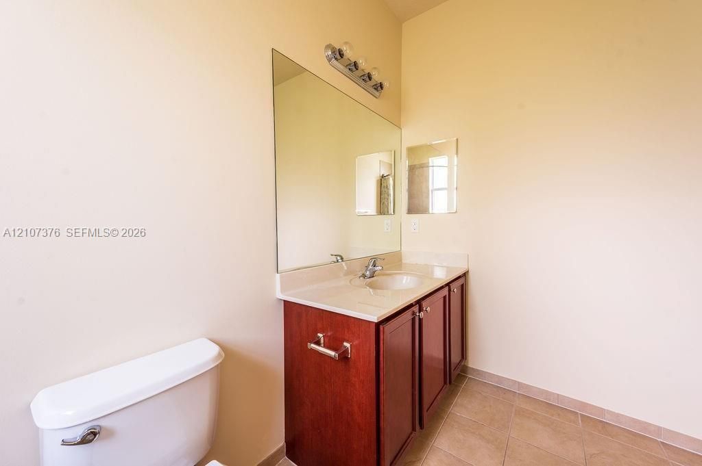 Vanity with solid-surface countertop and integrated sink, dark wood-finish cabinetry, full-width wall mirror, chrome faucet hardware, and ceramic tile flooring