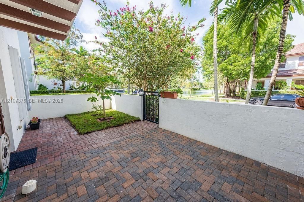 Enclosed patio featuring multi-toned brick pavers, a manicured lawn patch, decorative stucco privacy walls, and a metal gate