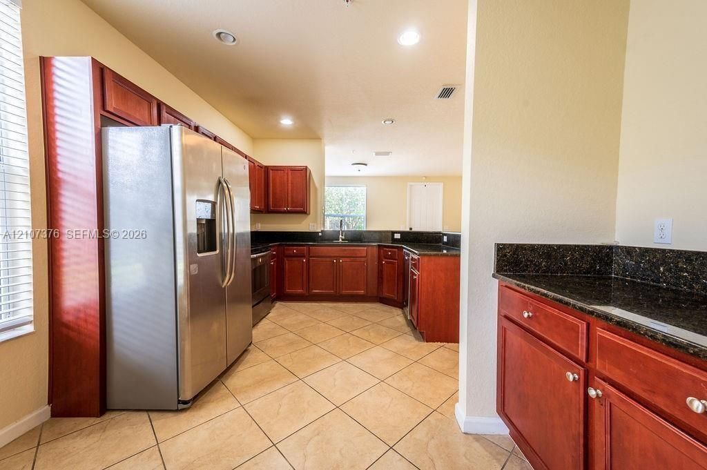 Kitchen featuring custom cherry-toned cabinetry, dark stone countertops, stainless steel appliances, and ceramic tile flooring