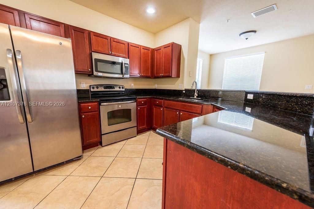 Kitchen featuring dark-toned cabinetry, stone-finish countertops, stainless steel appliances, and ceramic tile flooring