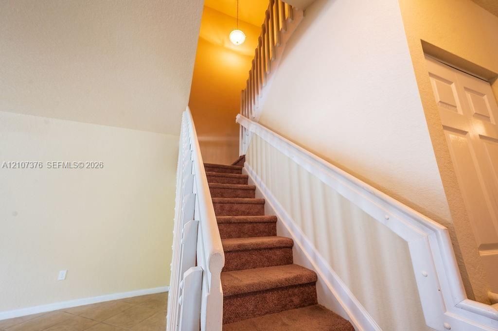 Staircase featuring carpeted treads, white painted wooden balusters and railings, and a suspended globe pendant light