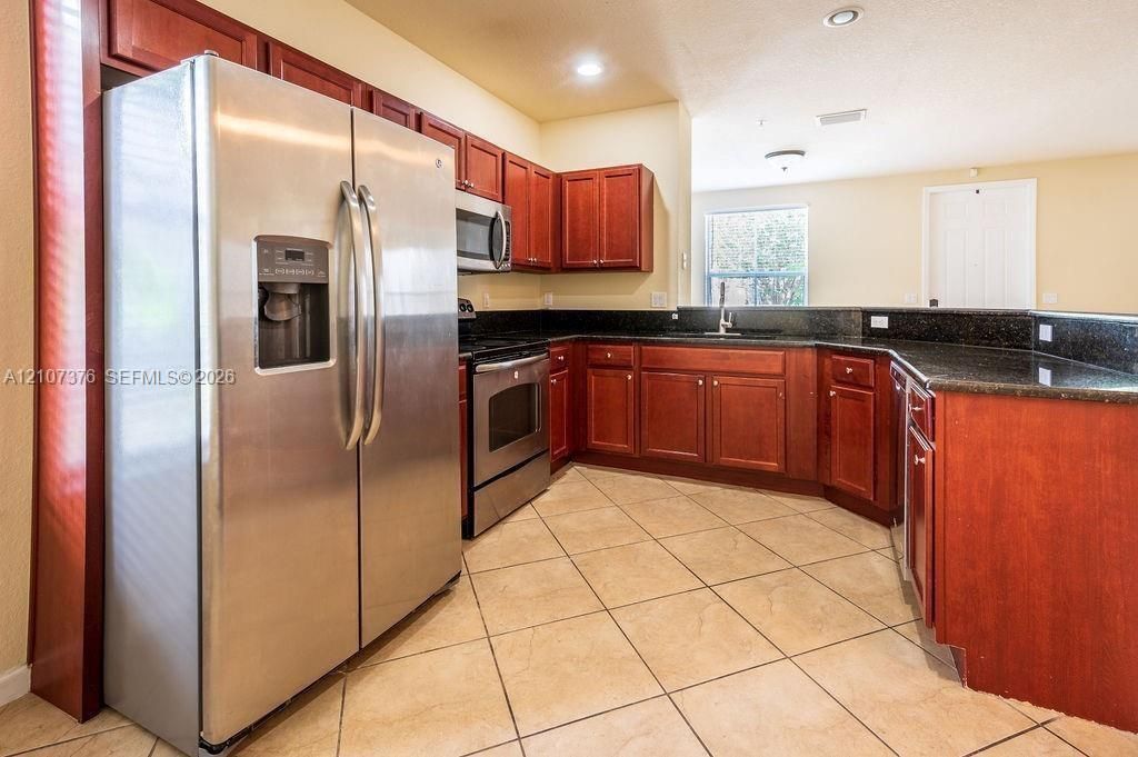 Kitchen featuring wood cabinetry, stainless steel appliances, dark countertops, tiled flooring, and recessed lighting