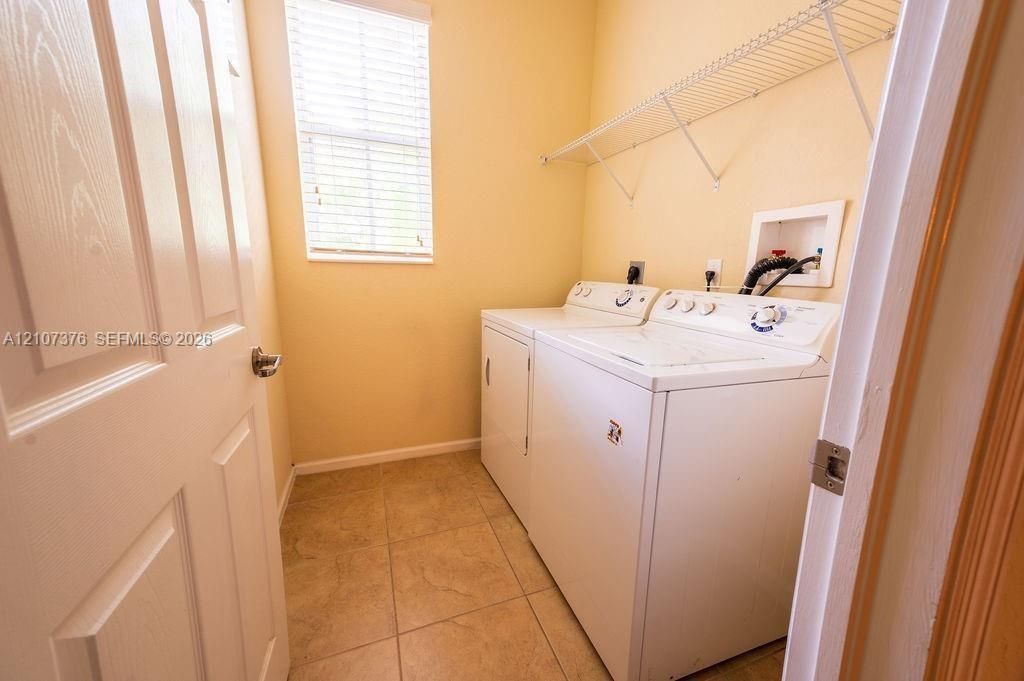 Laundry space featuring tiled flooring, a single window with horizontal blinds, and a built-in wire shelving unit