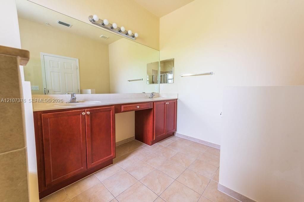 Dual-sink vanity with wood cabinetry, integrated countertop, full-width wall mirror, and five-bulb vanity light fixture, complemented by tile flooring