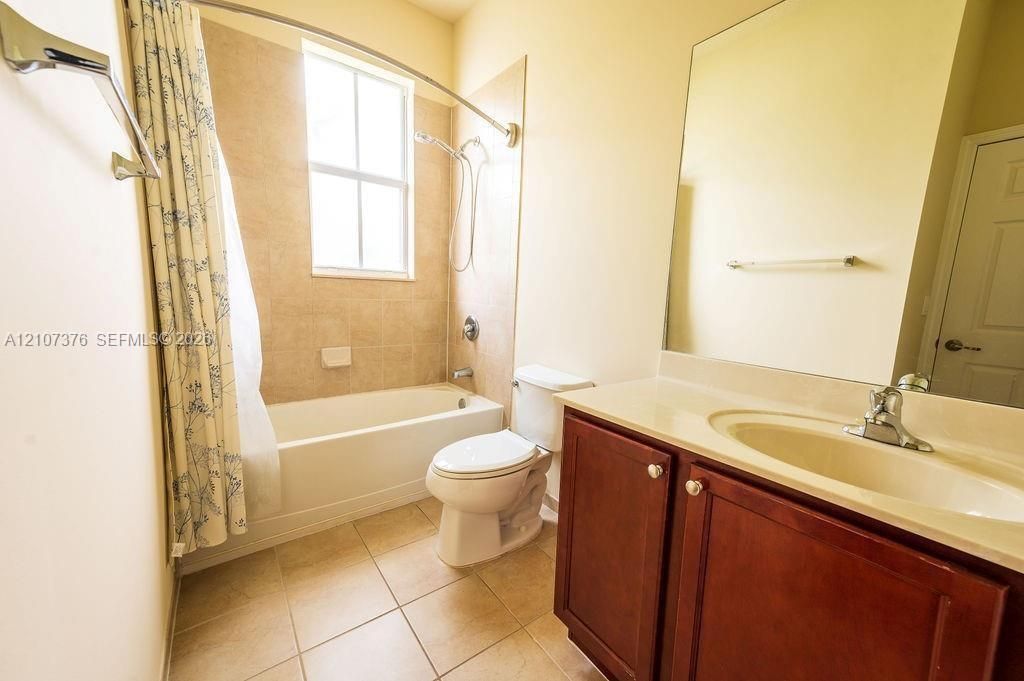 Bathroom featuring a vanity with wood-finish cabinetry, a tub-shower combination with tiled surround, a large wall-mounted mirror, and tile flooring