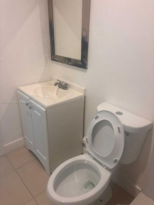 White vanity with integrated sink, two-door storage cabinet, chrome faucet, wall-mounted mirror, and tile flooring