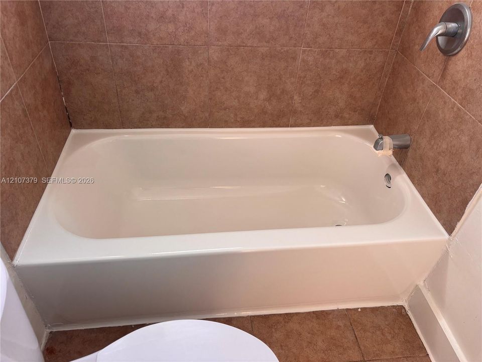 Bathtub featuring integrated surround, earth-tone ceramic tile wall cladding, and chrome-finish fixtures