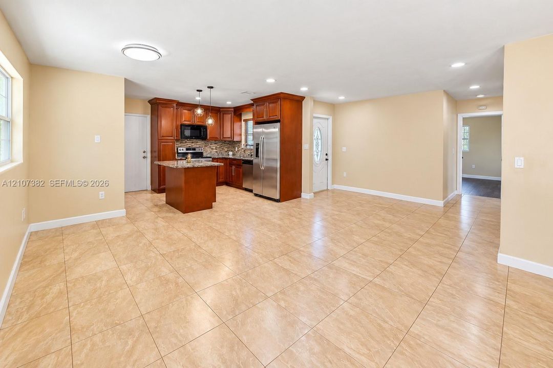 Kitchen featuring wood cabinetry, stone-finish countertops, stainless steel appliances, a center island, and neutral tile flooring