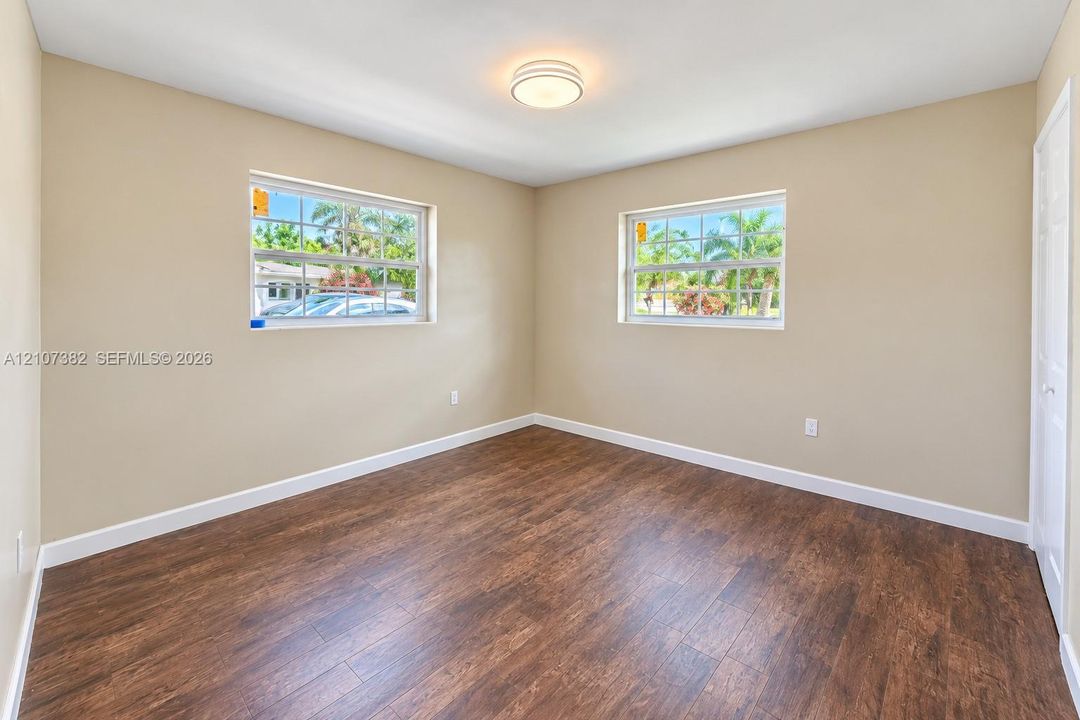 Room featuring wood-finish flooring, dual windows with grid detailing, neutral wall tones, and a central flush-mount ceiling light fixture