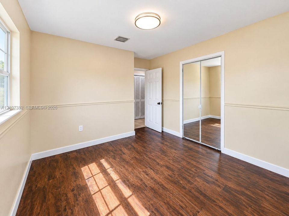 Wood-finish flooring, dual-panel sliding mirror closet doors, chair rail molding, and a flush-mount ceiling light fixture