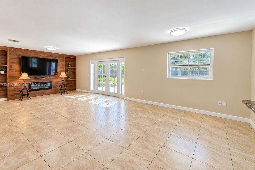 Spacious interior featuring large-format tile flooring, built-in wood-finish cabinetry, a sleek electric fireplace, and double-pane French doors