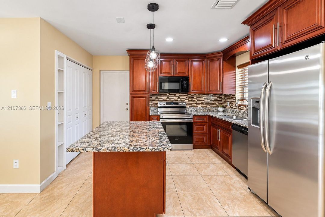 Kitchen featuring raised-panel wood cabinetry, stone countertops, stainless steel appliances, multi-toned stone tile backsplash, and ceramic tile flooring