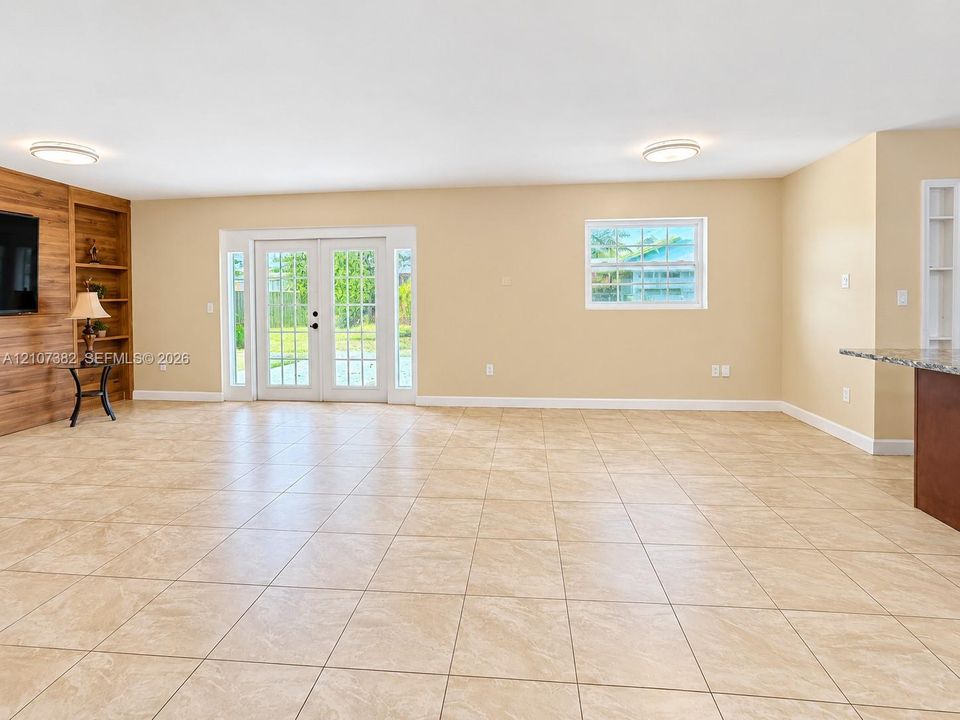 Tile flooring, wood-finish wall accent with integrated shelving, double French doors, and recessed ceiling lighting