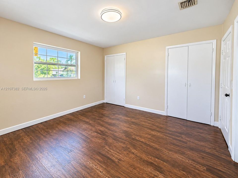 Interior room featuring wood-finish flooring, dual built-in closets with white paneled doors, and a multi-pane window