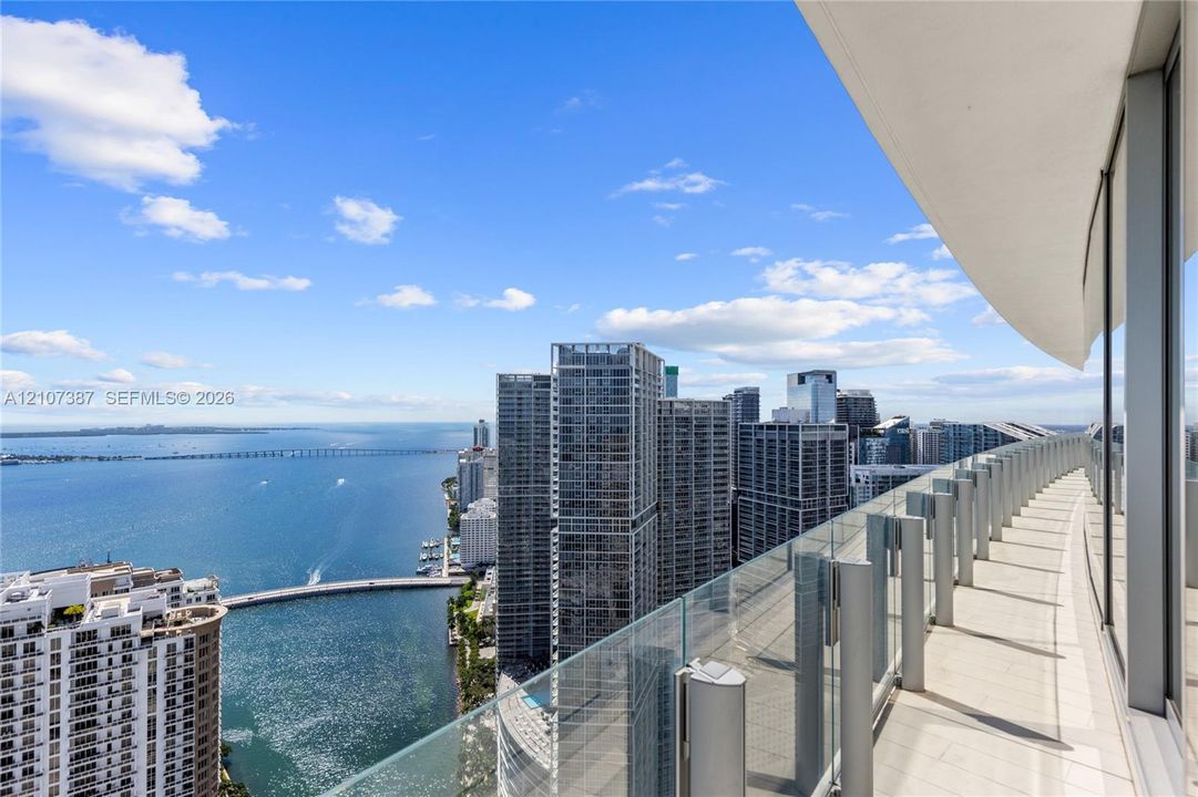 Expansive wraparound balcony featuring large-format tile flooring, a sleek glass railing, and a covered overhead soffit