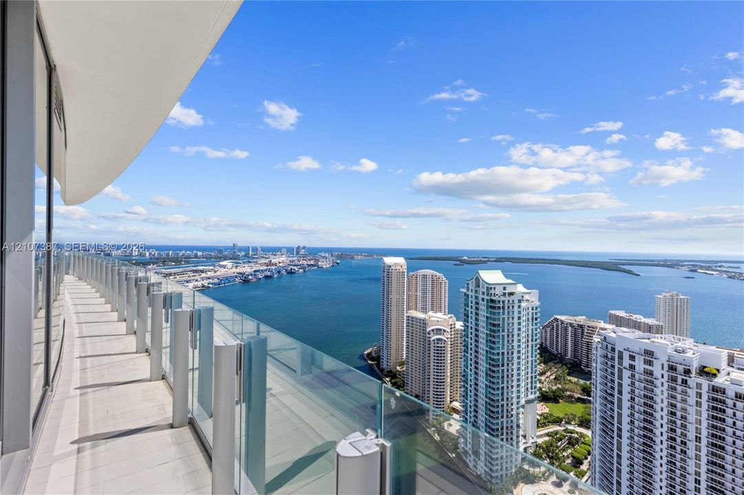Curved wrap-around balcony featuring glass panel railing, tile flooring, and expansive water and urban skyline scenery