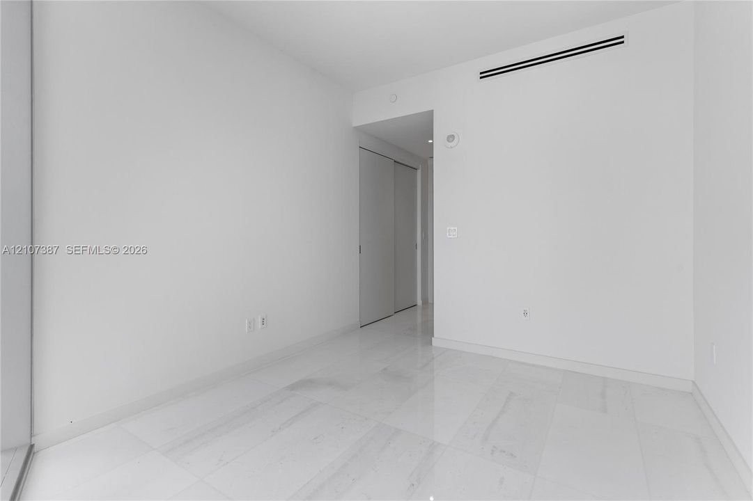 Minimalist interior space featuring polished light-toned stone flooring and dual-panel sliding closet doors