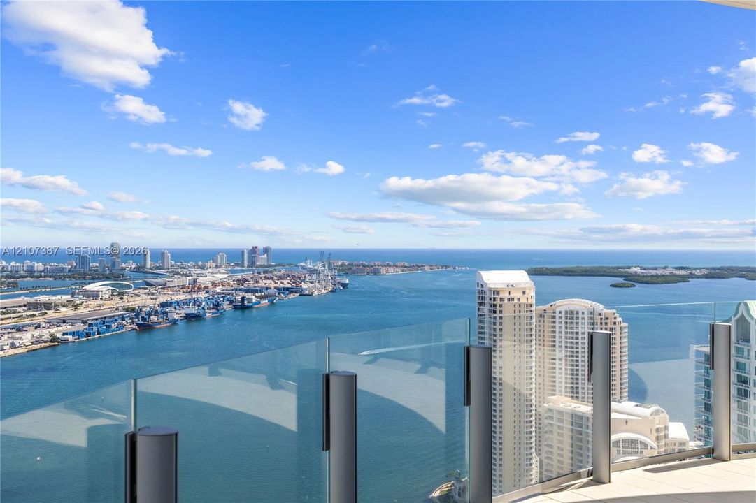 Expansive balcony featuring frameless glass railings and paved flooring, showcasing a panoramic coastal, harbor, and cityscape backdrop