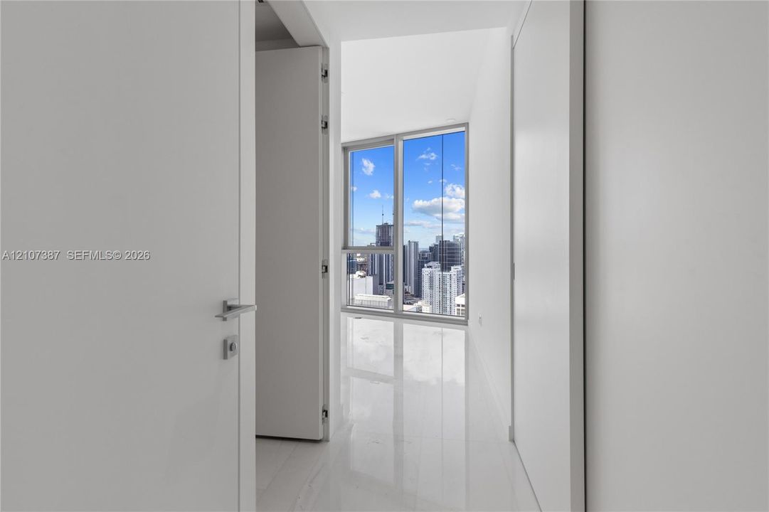 Bright interior hallway featuring polished stone flooring, floor-to-ceiling window, urban skyline backdrop, and minimalist smooth-finish white doors