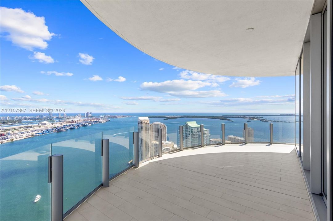 Curved balcony featuring tile flooring, glass panel railings, and panoramic coastal and urban scenery