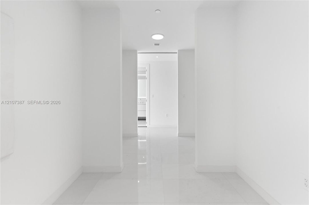 Interior corridor featuring polished stone-finish tile flooring, clean white walls, and recessed ceiling lighting