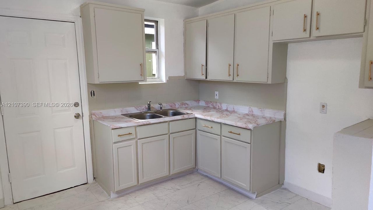 Kitchen area featuring shaker-style cabinetry, stone-patterned countertops, a dual-basin stainless steel sink with a high-arch faucet, and light-toned tile flooring