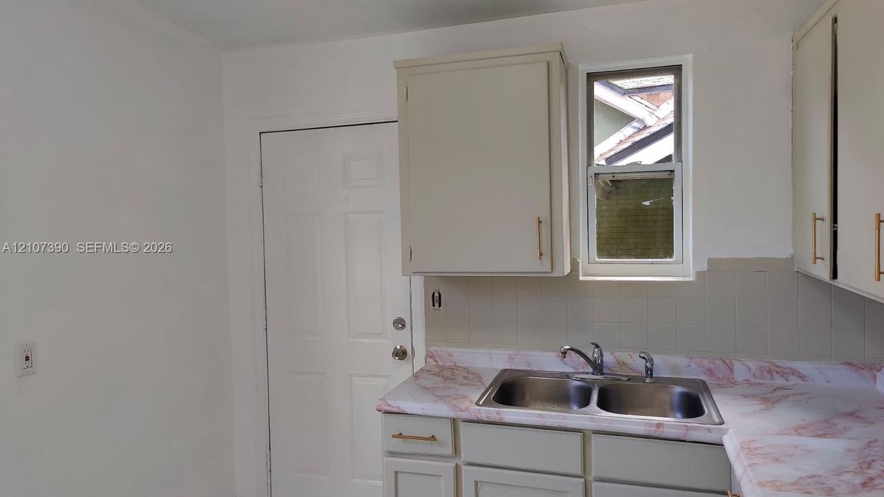 Kitchen featuring cabinetry with metallic hardware, a double-basin stainless steel sink with a faucet, laminate countertops, and a window