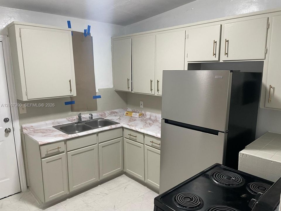 Kitchen featuring light-toned cabinetry with metal hardware, stone-patterned countertops, a dual-basin stainless steel sink, and a refrigerator