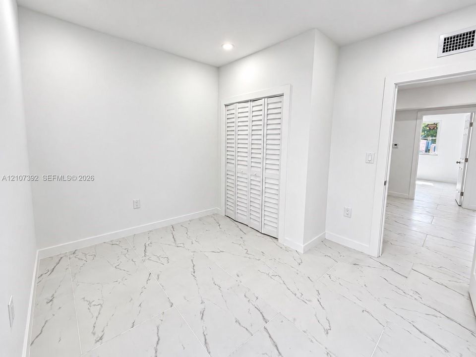 Neutral-toned interior featuring large-format tile flooring with veined detailing and a built-in closet with white louvered bifold doors