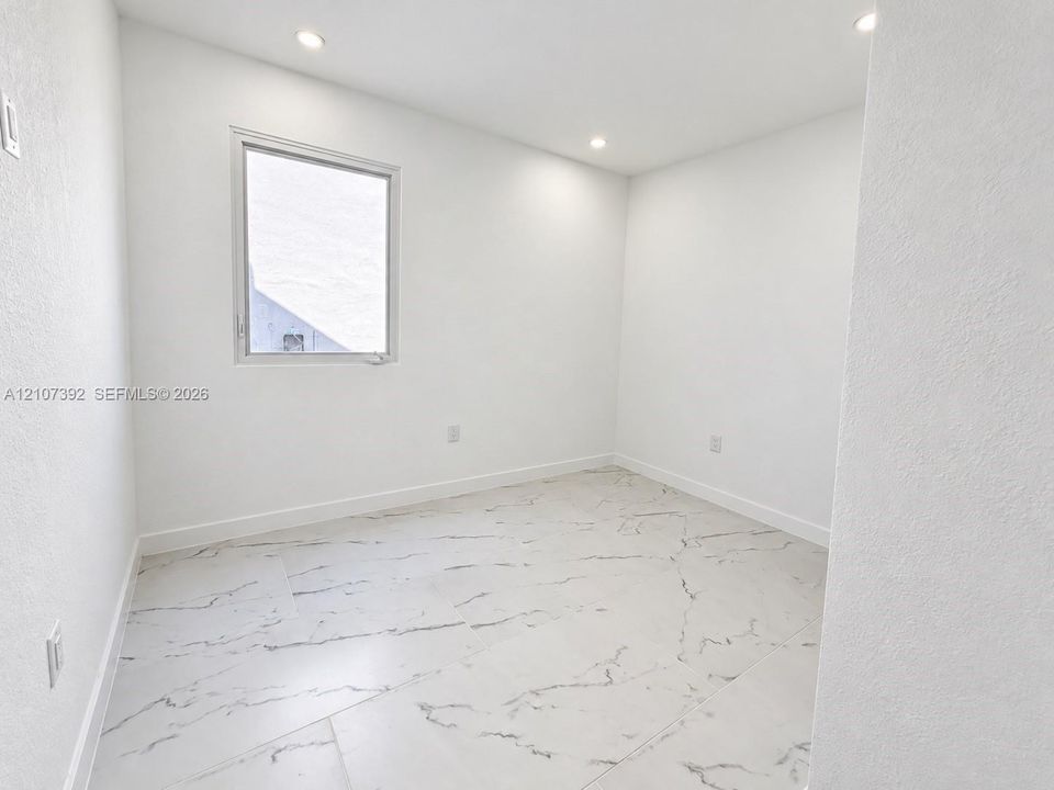 Room featuring large-format tile flooring with veining, recessed lighting, and a single-pane window