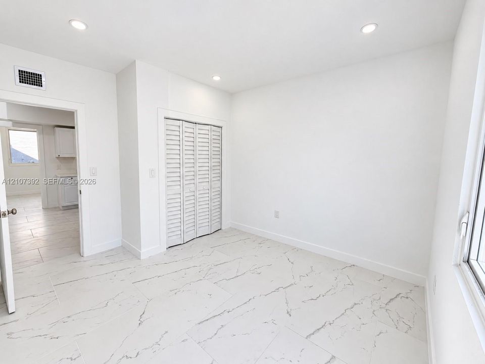 Neutral-toned interior featuring stone-finish floor tiling, recessed lighting, and a bi-fold closet with louvered doors