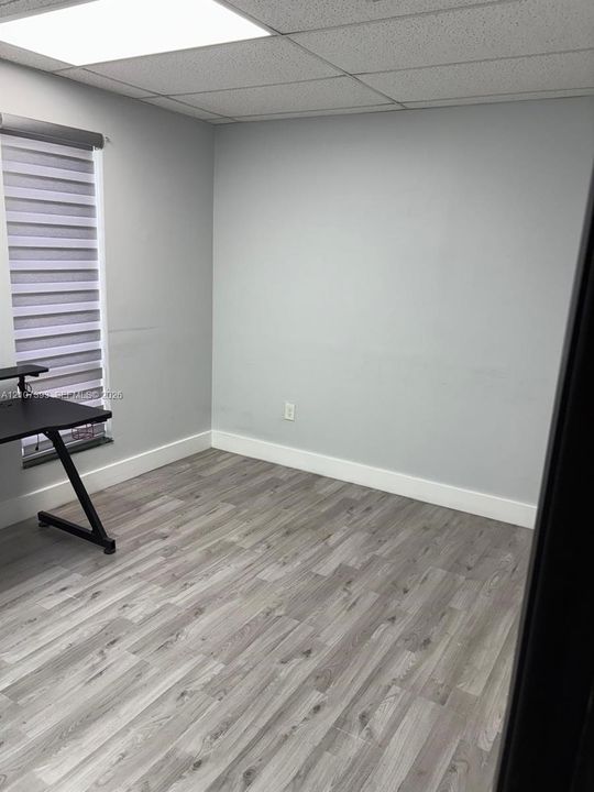Neutral-toned room featuring wood-finish flooring, a drop ceiling with recessed lighting, and a window with installed roller shades