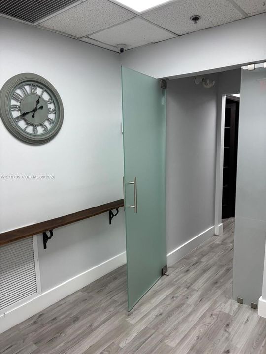 Frosted glass pivot door with stainless steel handle, wood-finish flooring, and wall-mounted dark wood shelf featuring iron brackets
