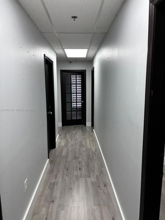 Hallway featuring wood-finish flooring, drop ceiling with recessed lighting, and a dark-framed multi-pane glass door