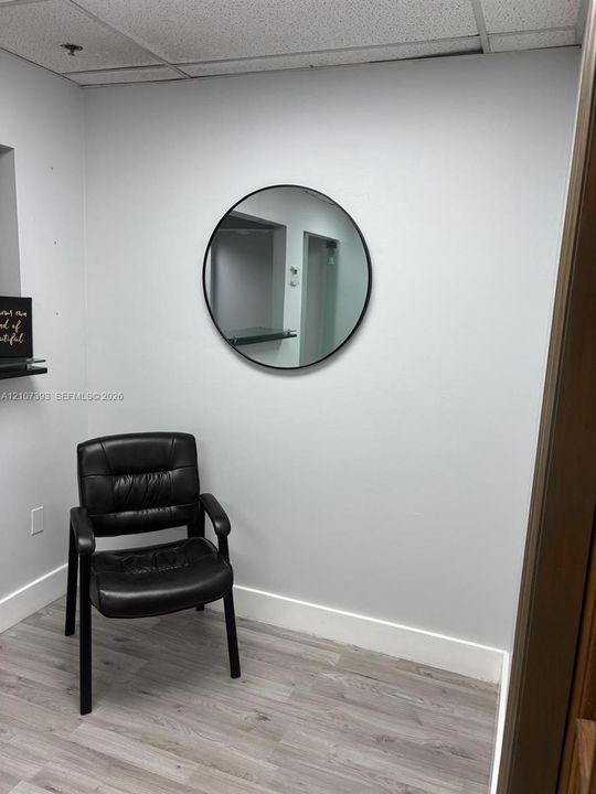 Neutral-toned wood-finish flooring with a circular mirror featuring a black frame and a wall-mounted floating glass shelf
