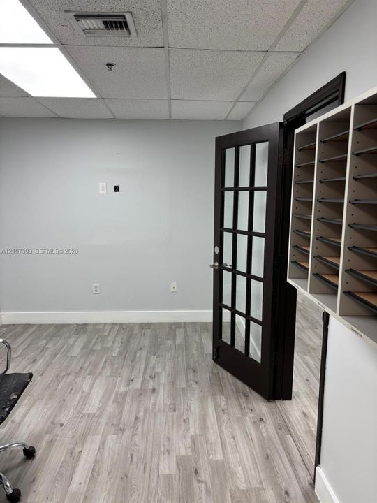 Interior space featuring wood-finish flooring, a dark-toned door with glass panes, and built-in tiered storage shelving