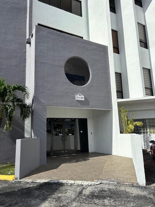 Exterior entrance featuring a concrete facade, circular accent window, paved brick walkway, and glass-paned double doors