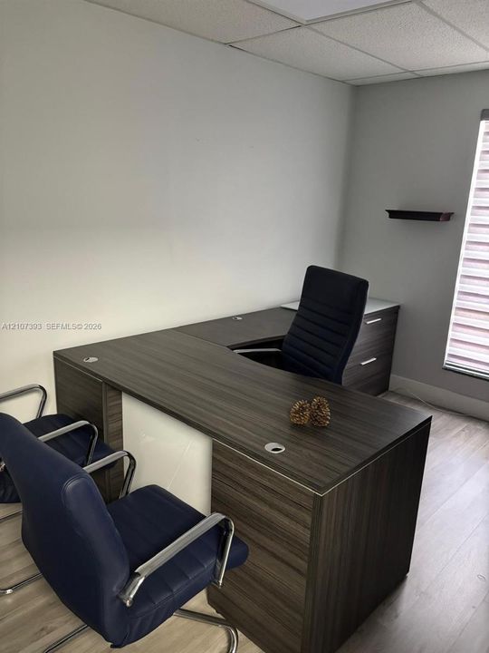 Neutral-toned room featuring wood-finish flooring, a wall-mounted display shelf, and a window with horizontal blinds