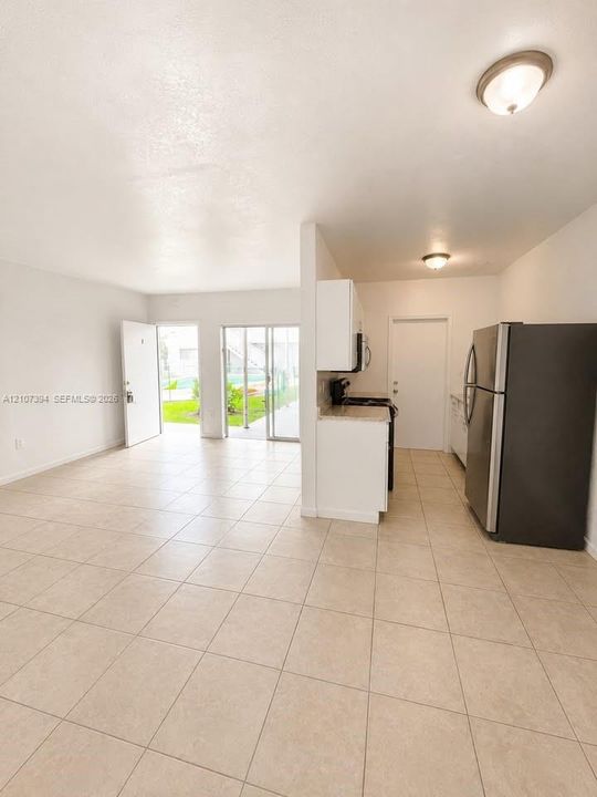 Ceramic tile flooring, white cabinetry, solid-surface countertops, stainless steel refrigerator, and glass sliding door access to exterior space