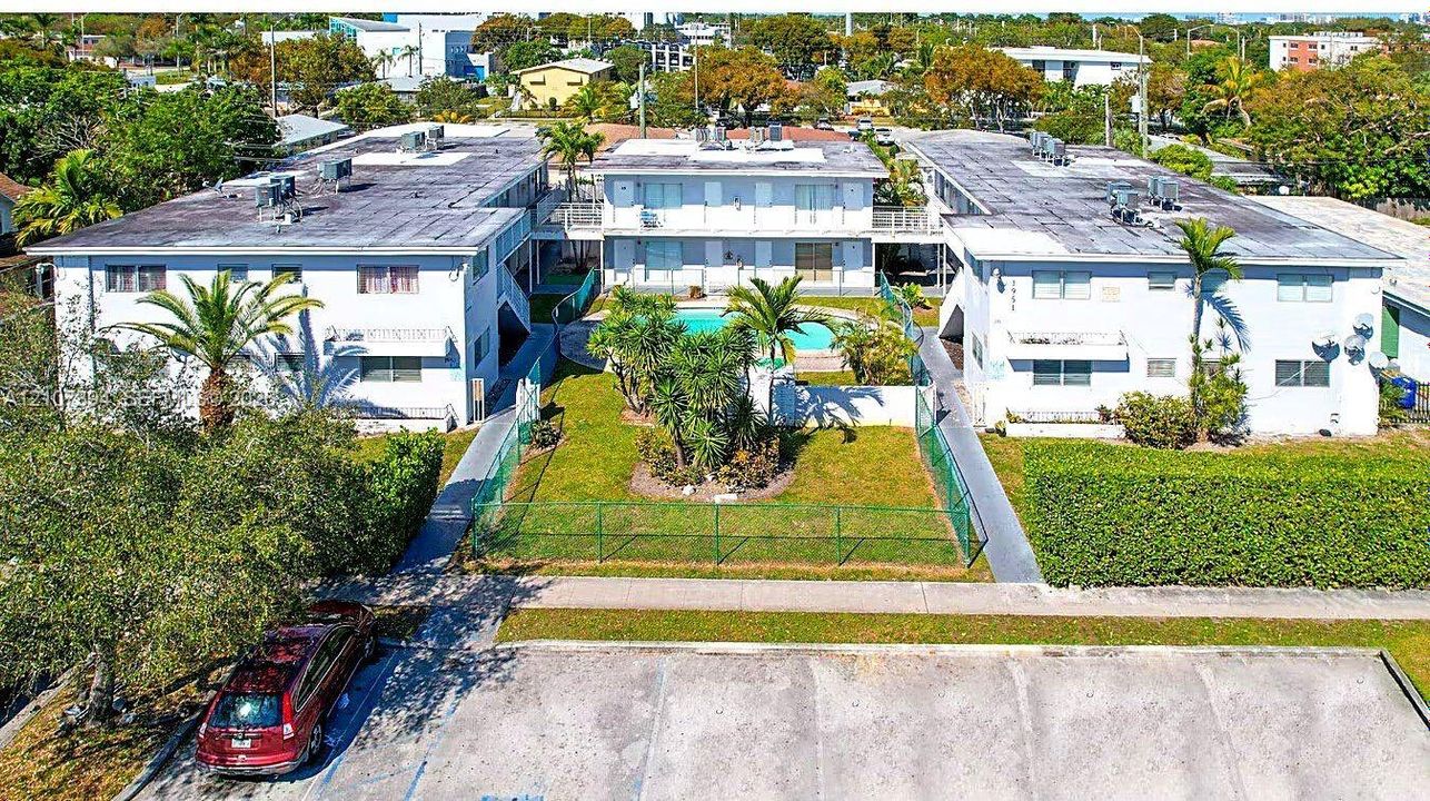 Multi-story residential complex featuring a central swimming pool, paved surface parking, and perimeter landscaping